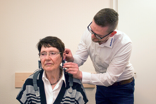 Hörtest bei älterer Frau durch Hörakustiker in moderner Hörgeräteakustik Praxis.